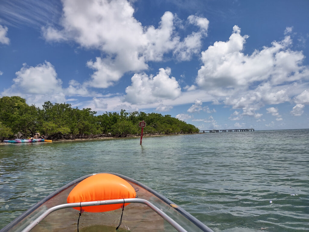 Blue skies with soft clouds over clear water as a kayak heads to Indian Key in the kayak the Florida Keys guide.
