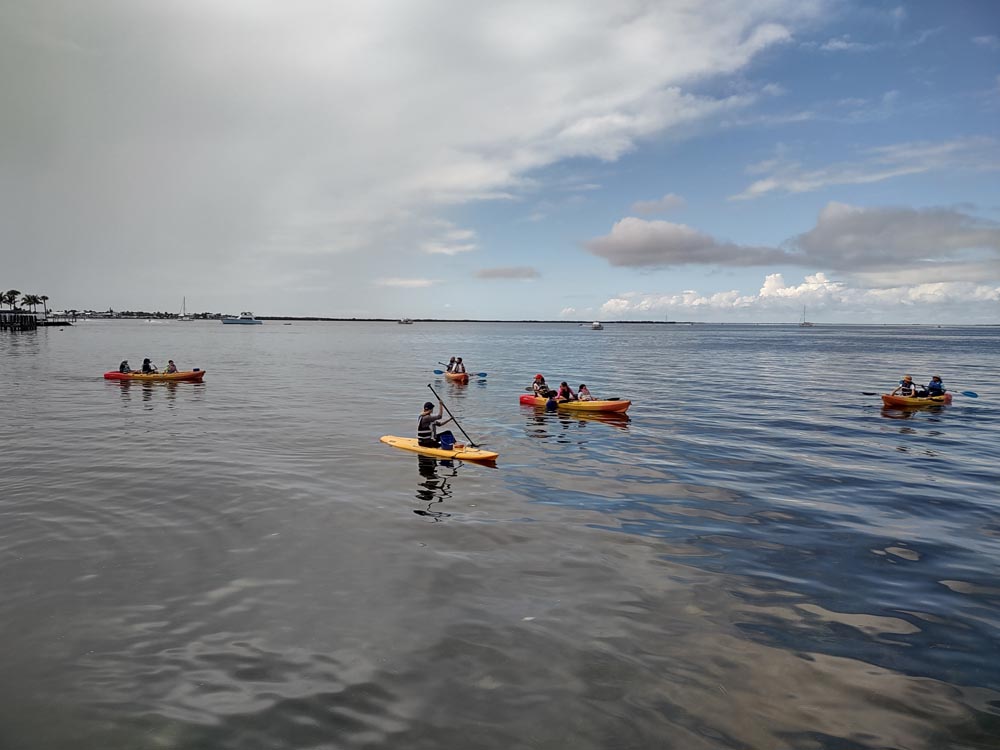  A group of kayaks and paddleboards float on the calm waters of Blackwater Sound in Key Largo Florida, under a cloudy blue sky.