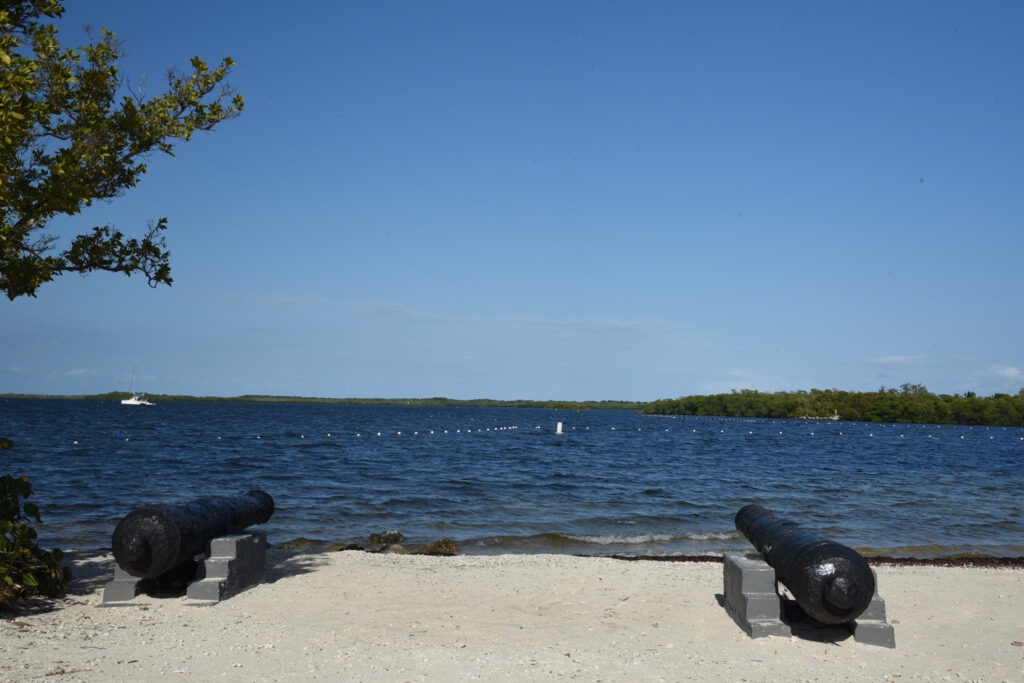 Two canons sitting on the sandy beach aim out over the blue waters of the Largo Sound in Key Largo Florida.