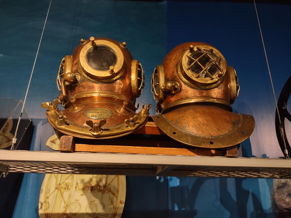 Two brass dive helmets sit on a shelf in an exhibit at the History of Diving Museum.