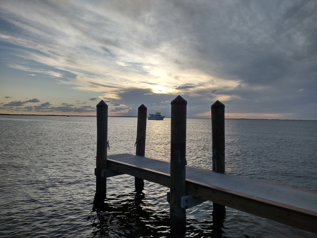 A cabin boat is seen beyond a pier as the sunsets behind a cloud in Key Largo.