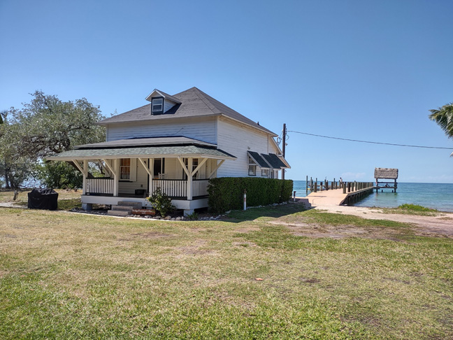 An early 1900s craftsman style home on Pigeon Key.  The white clapboard siding two story house with a porch across the front sits on the edge of the Caribbean colored water.