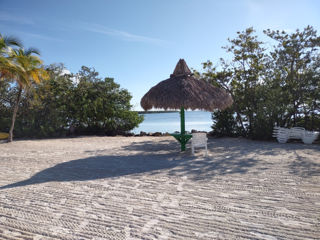 A small round table under a thatched roof looks over the blue waters of Blackwater Sound in one of the best beaches of the Florida Keys.