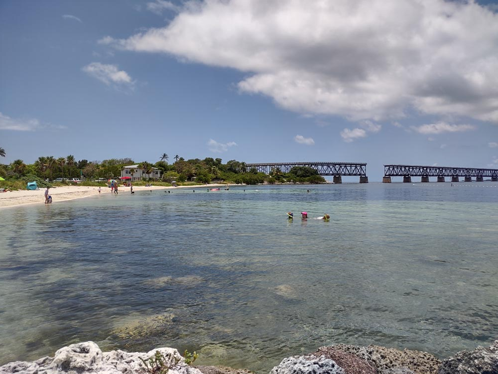 People float in the cleat waters at the beach at Bahia Honda. The abandoned Overseas Railway bridge in the distance at one of the best beaches in the Florida Keys..