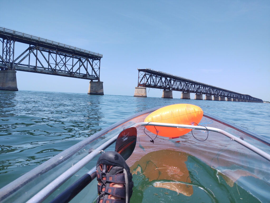 The Bahia Honda Bridge is on the horizon with a kayak floating in the water below.  The sandal in the kayak is part of the Florida Keys packing list.