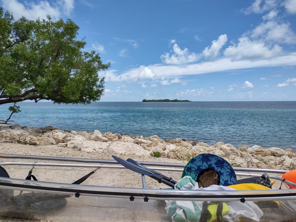 A kayak loaded with a colorful wide brimmed hat and gear bag on the shore looking across to Indian Key in the Florida Keys